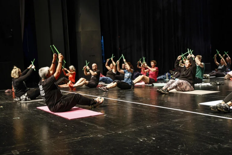 Gruppe von Personen führt gemeinsam eine Übung auf einer Bühne aus
