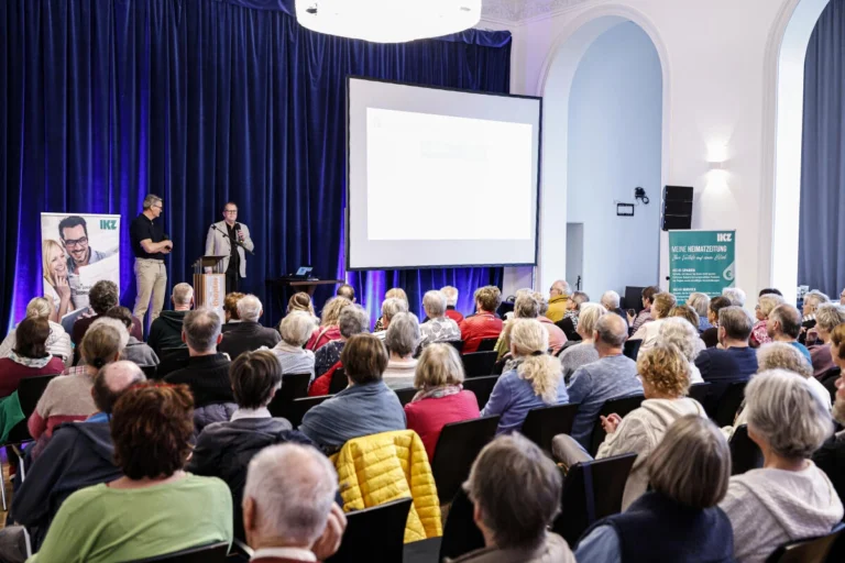 Publikum sitzt bei einem Vortrag vor einer Präsentationsfläche