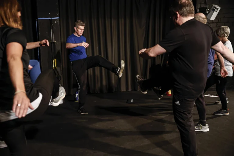 Personen trainieren zusammen mit dem Sportleiter auf einer dunklen Bühne