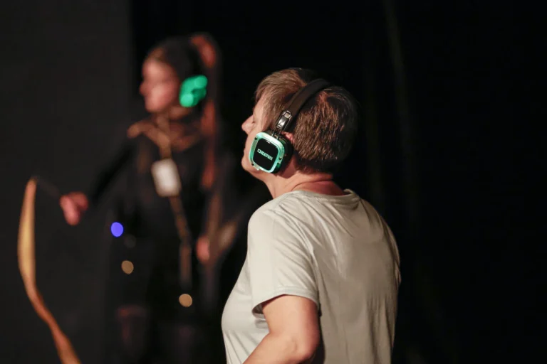Zwei Personen mit Kopfhörern stehen auf einer dunklen Bühne