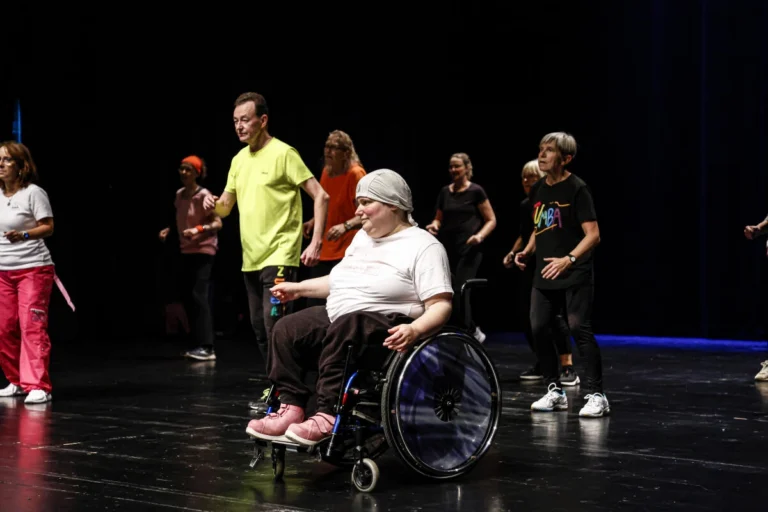 Mehrere Personen bewegen sich gemeinsam auf einer Bühne, darunter eine Person im Rollstuhl