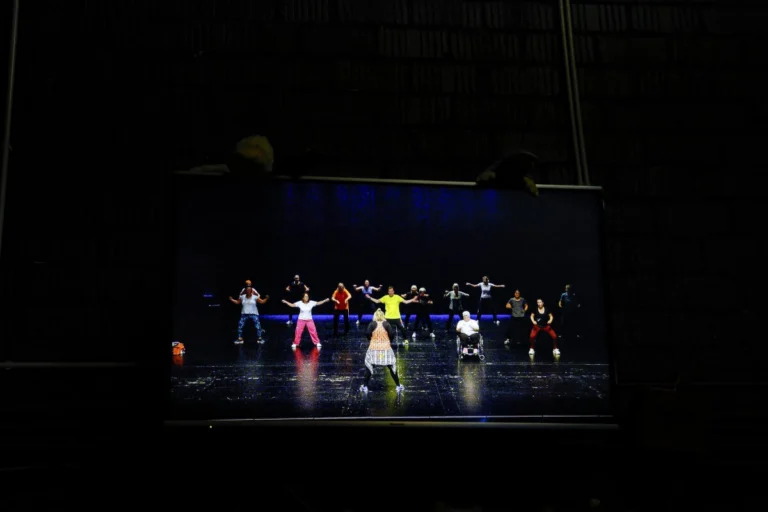 Gruppe an Personen führen eine sportliche Übung auf einer beleuchteten Bühne aus