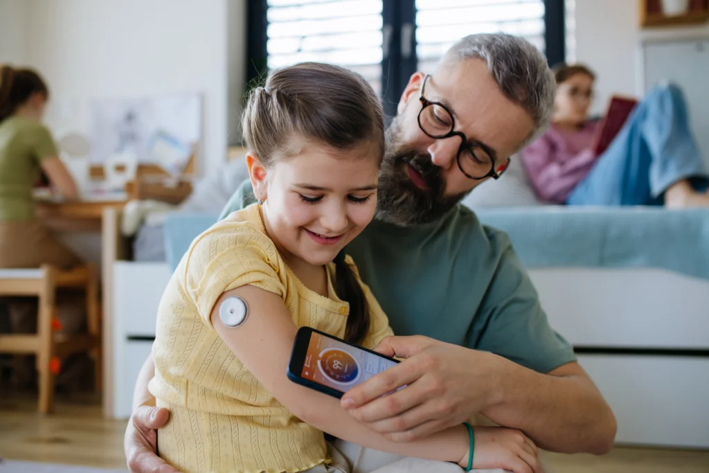 Kind sitz beim Papa auf dem Schoss und ermisst mit dem Handy den Zuckerwert des Kindes